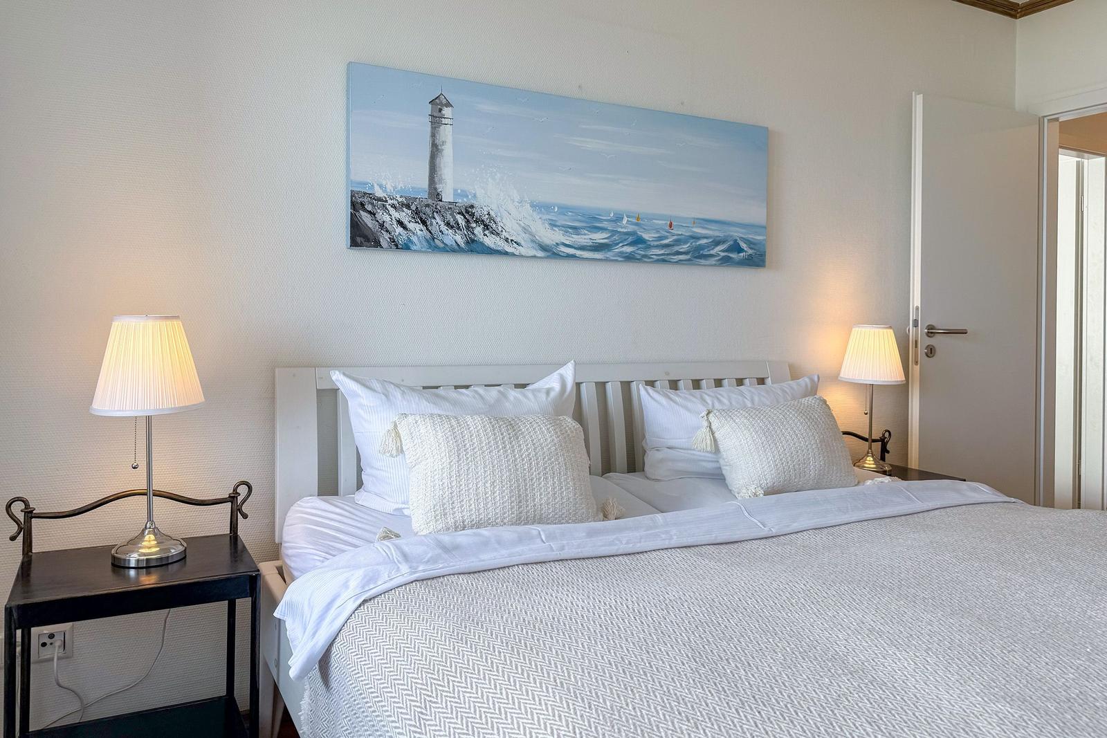 Schlafzimmer mit Bett, zwei Nachttischen und Wandbild mit Leuchtturm.