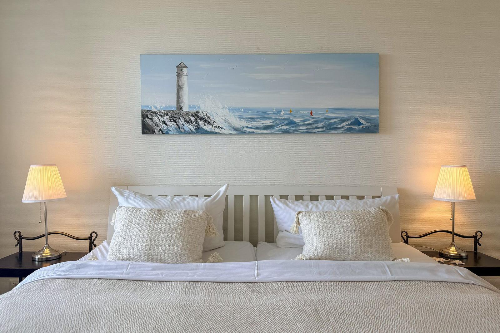 Doppelbett mit zwei Nachttischen und Lampen. Wandbild zeigt Leuchtturm und Meer.