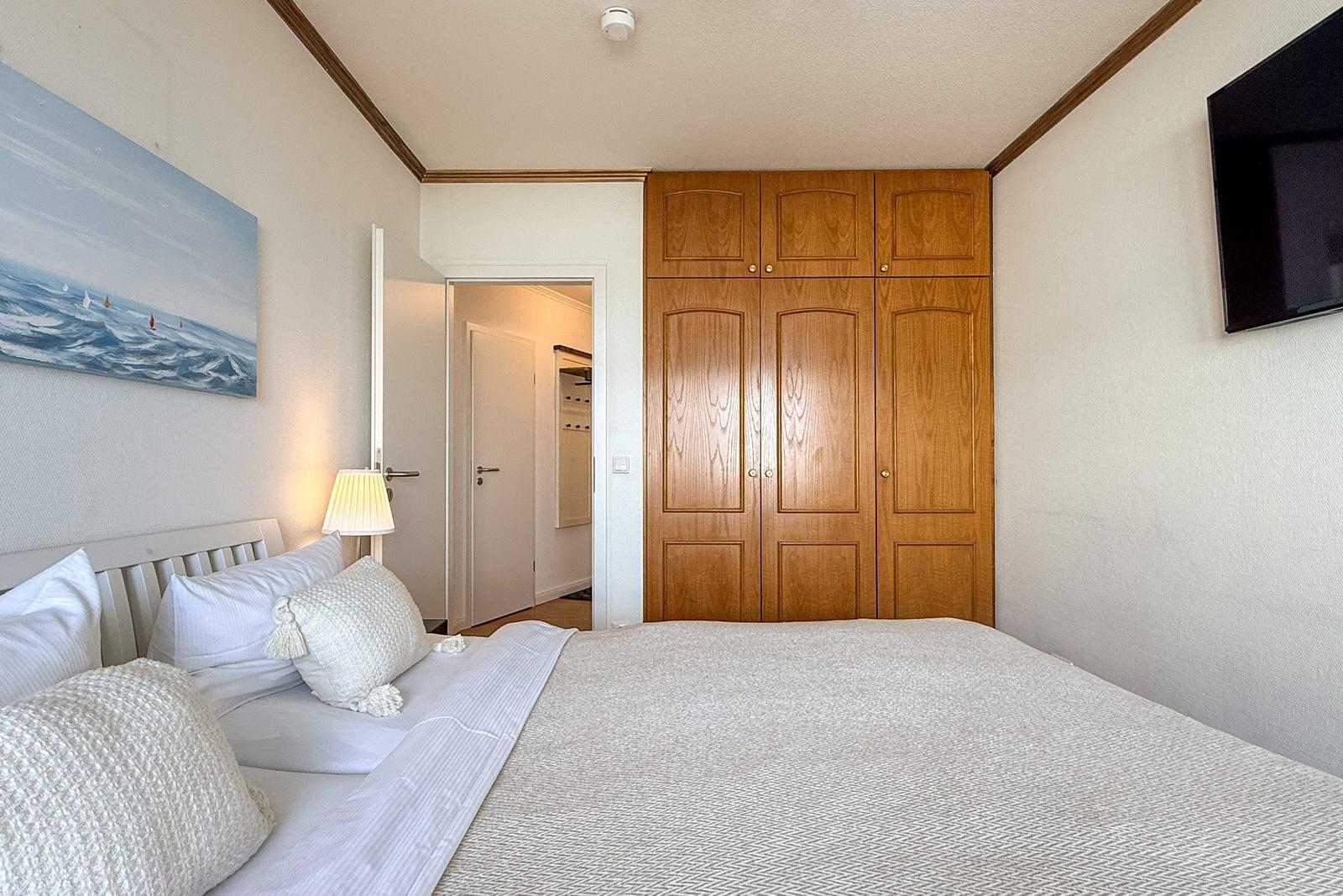 Schlafzimmer mit Bett, Kleiderschrank und Wandbild mit Segelbooten.