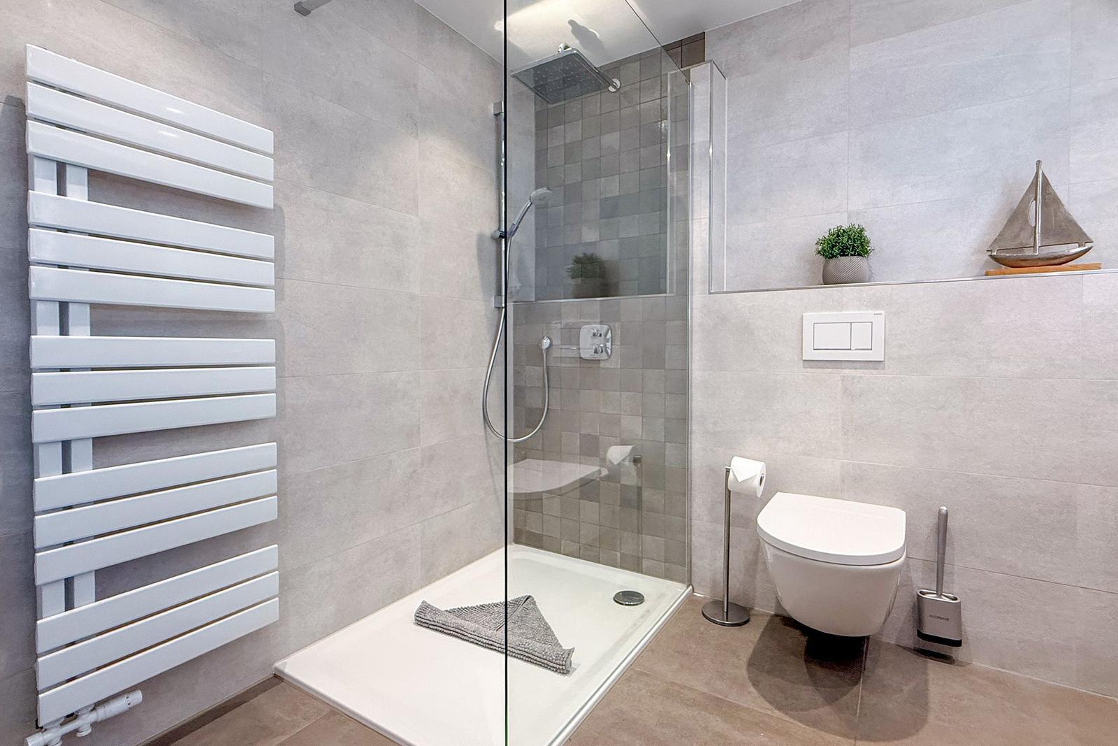 Dusche mit Glaswand, Toilette und Heizkörper an der Wand.