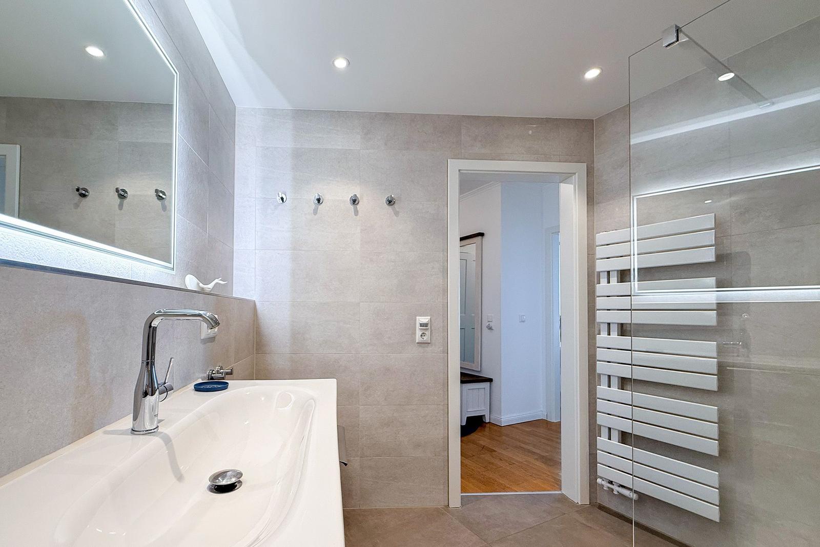 Badezimmer mit Waschbecken, Spiegel und Dusche mit Heizung.