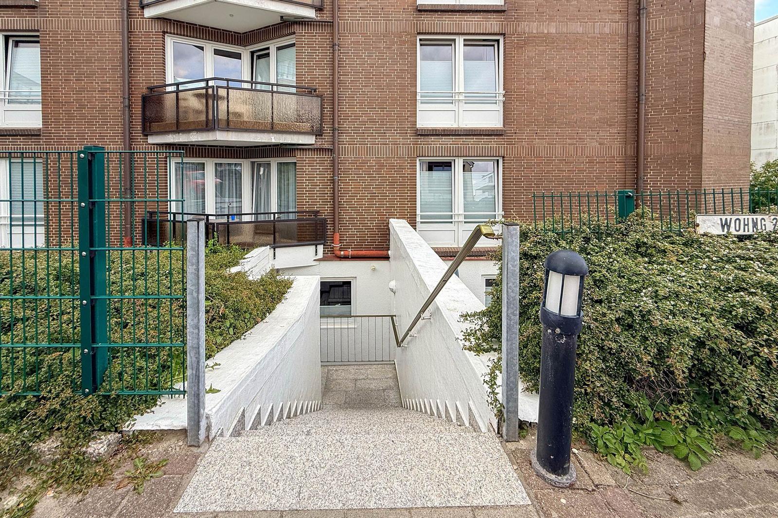 Haus mit Treppenaufgang, Geländer und grüner Hecke