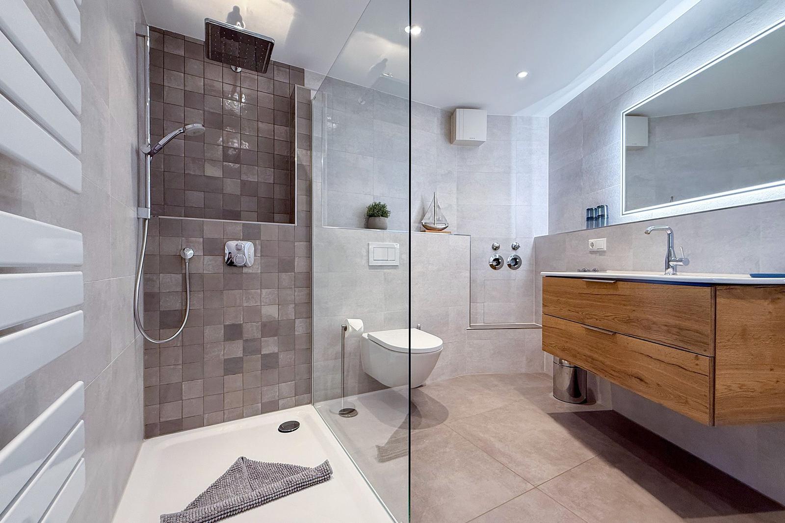 Dusche mit Regenduschkopf, Toilette und Waschtisch mit Spiegel.