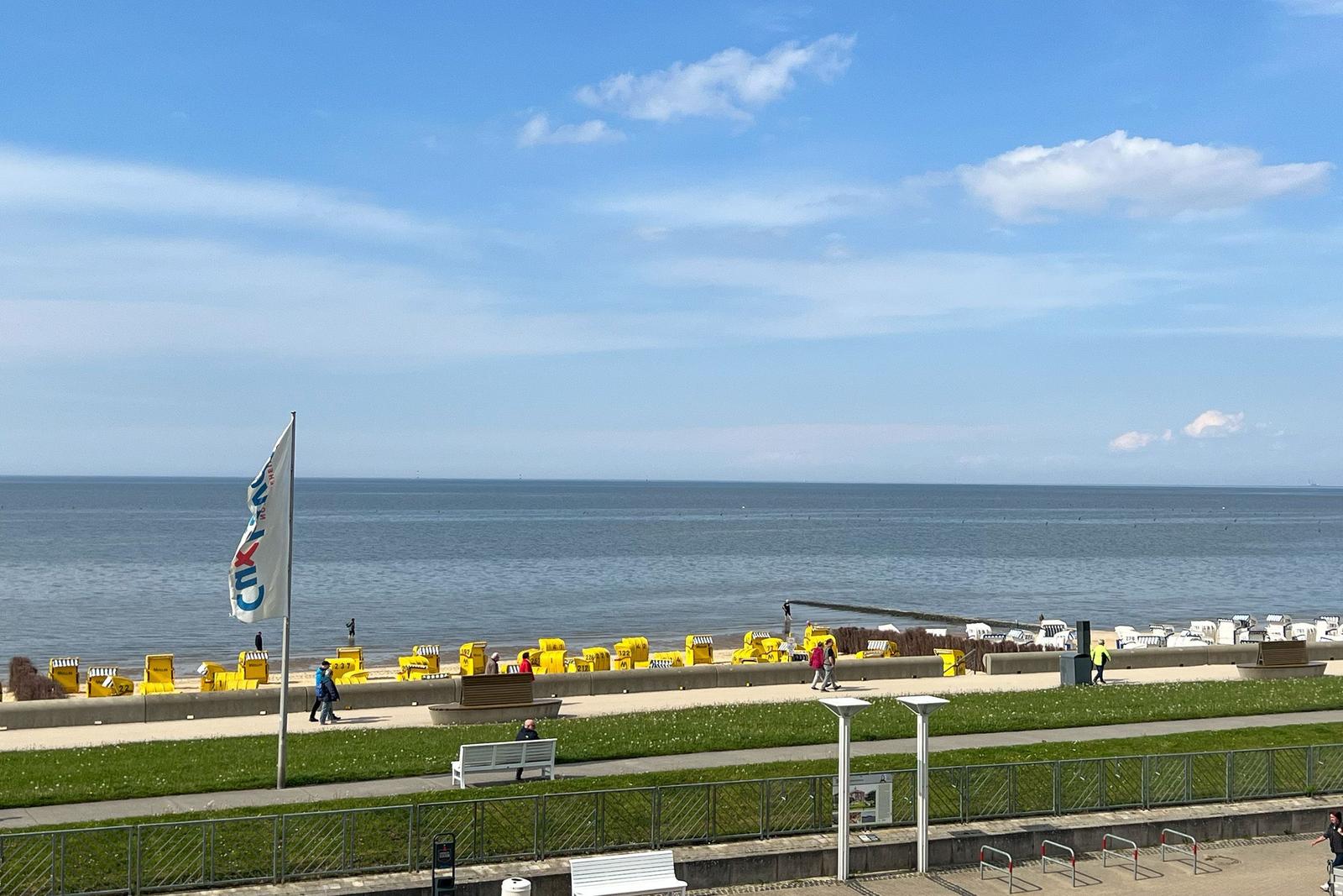 Meerfront mit Strandkörben und Promenade unter blauem Himmel.