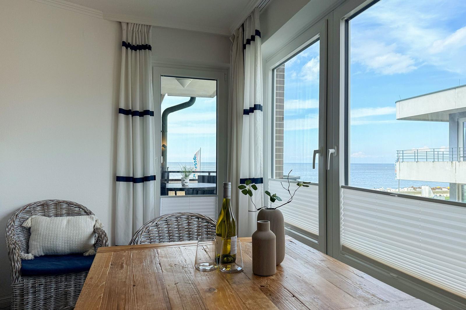 Esstisch mit Stühlen und Blick aufs Meer durch große Fenster.