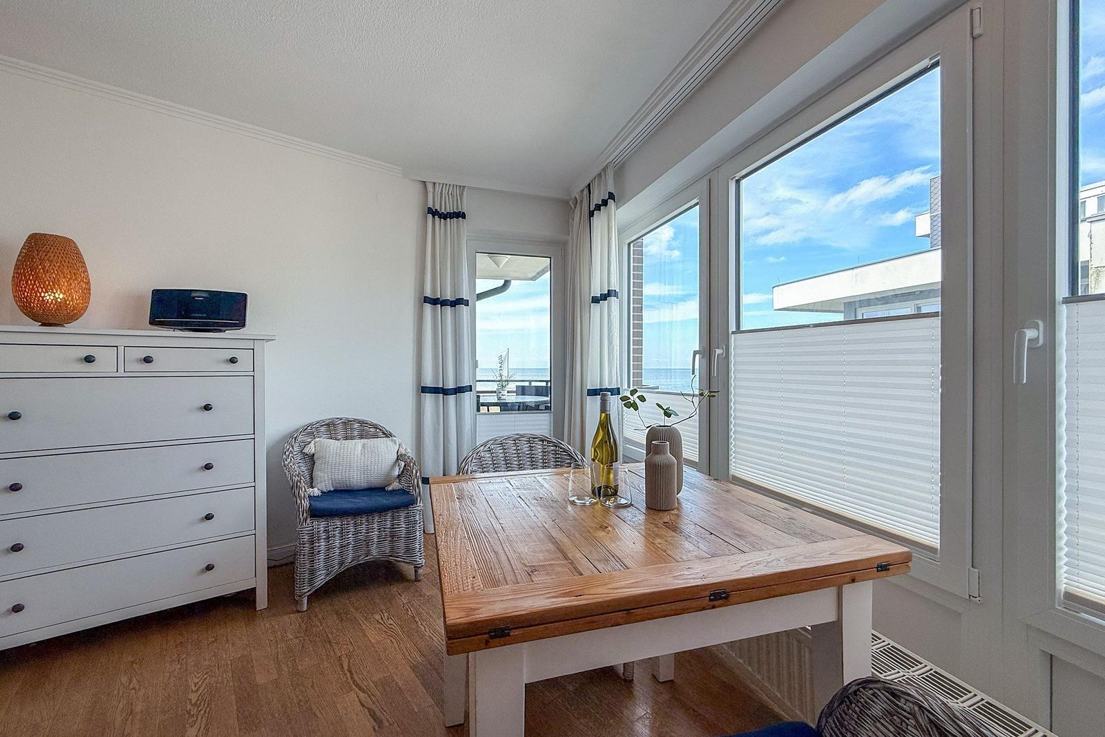 Esszimmer mit Holztisch, Stühlen und Blick auf Balkon. Hintergrund: weißer Schrank und Fenster.