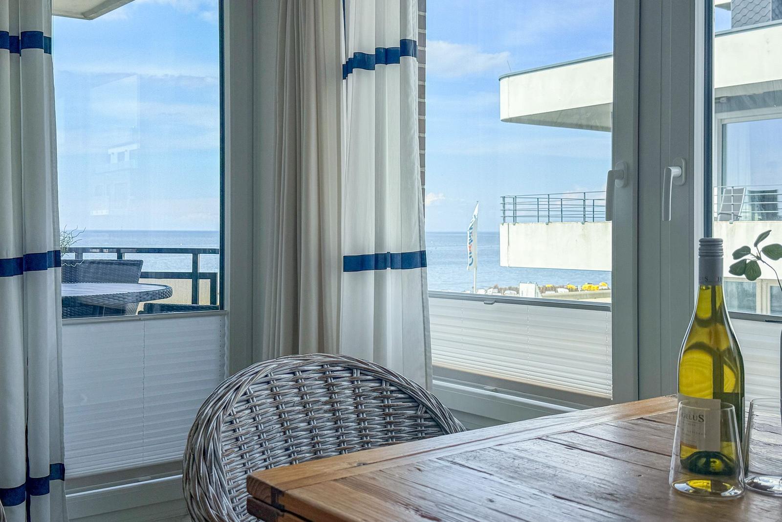 Tisch und Stuhl vor großem Fenster mit Meerblick und Terrasse.