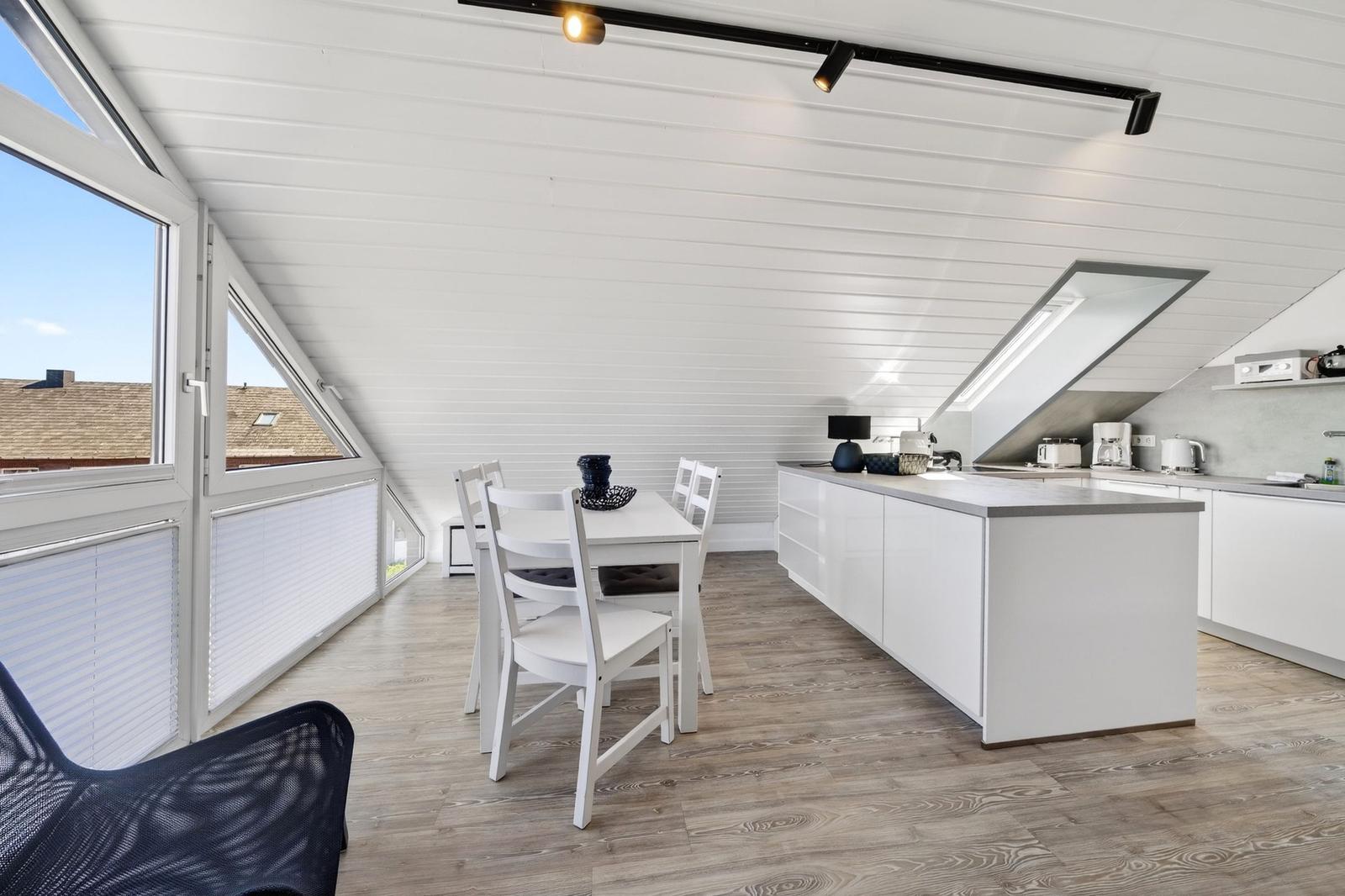 Küche mit Essbereich unter Dachschrägen, großes Fenster, weißer Tisch und Stühle.