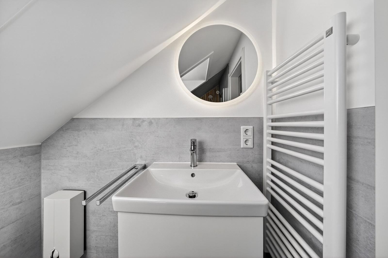 Badezimmer mit Waschbecken, runden Spiegel und Heizkörper