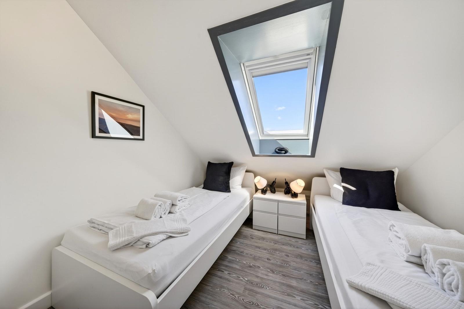Zwei Einzelbetten mit weißen Laken und Handtüchern unter einem Dachfenster.