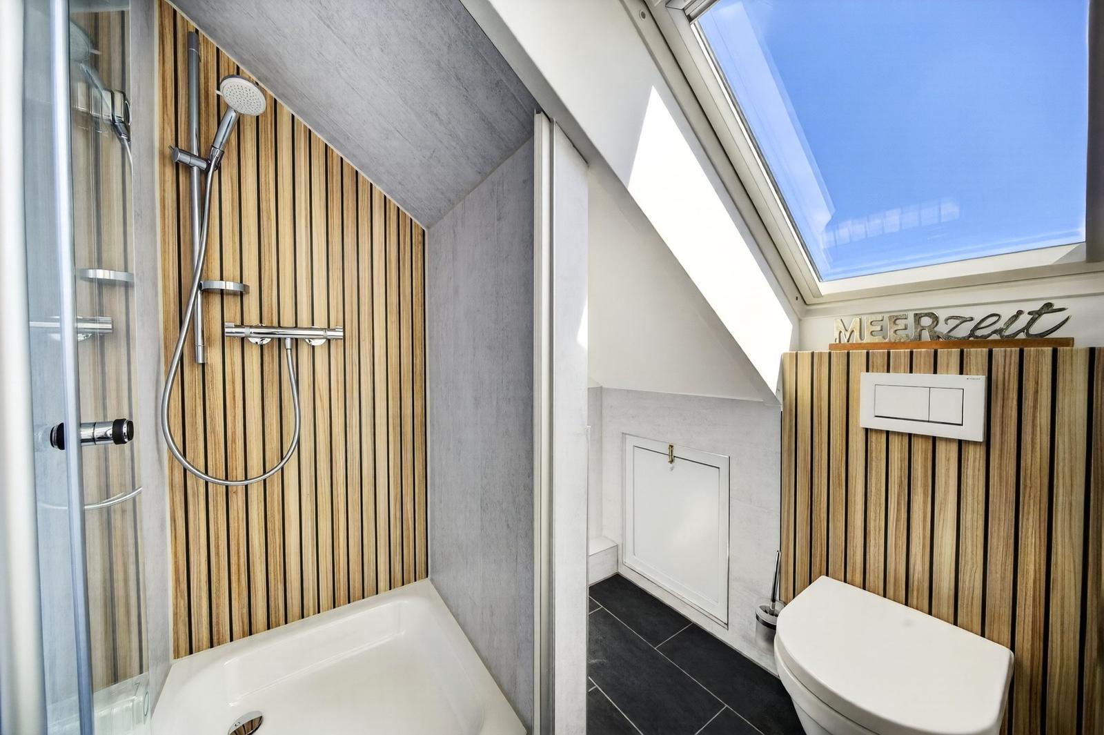 Dusche mit Holzwand und Toilette unter Dachschrägen mit Dachfenster.