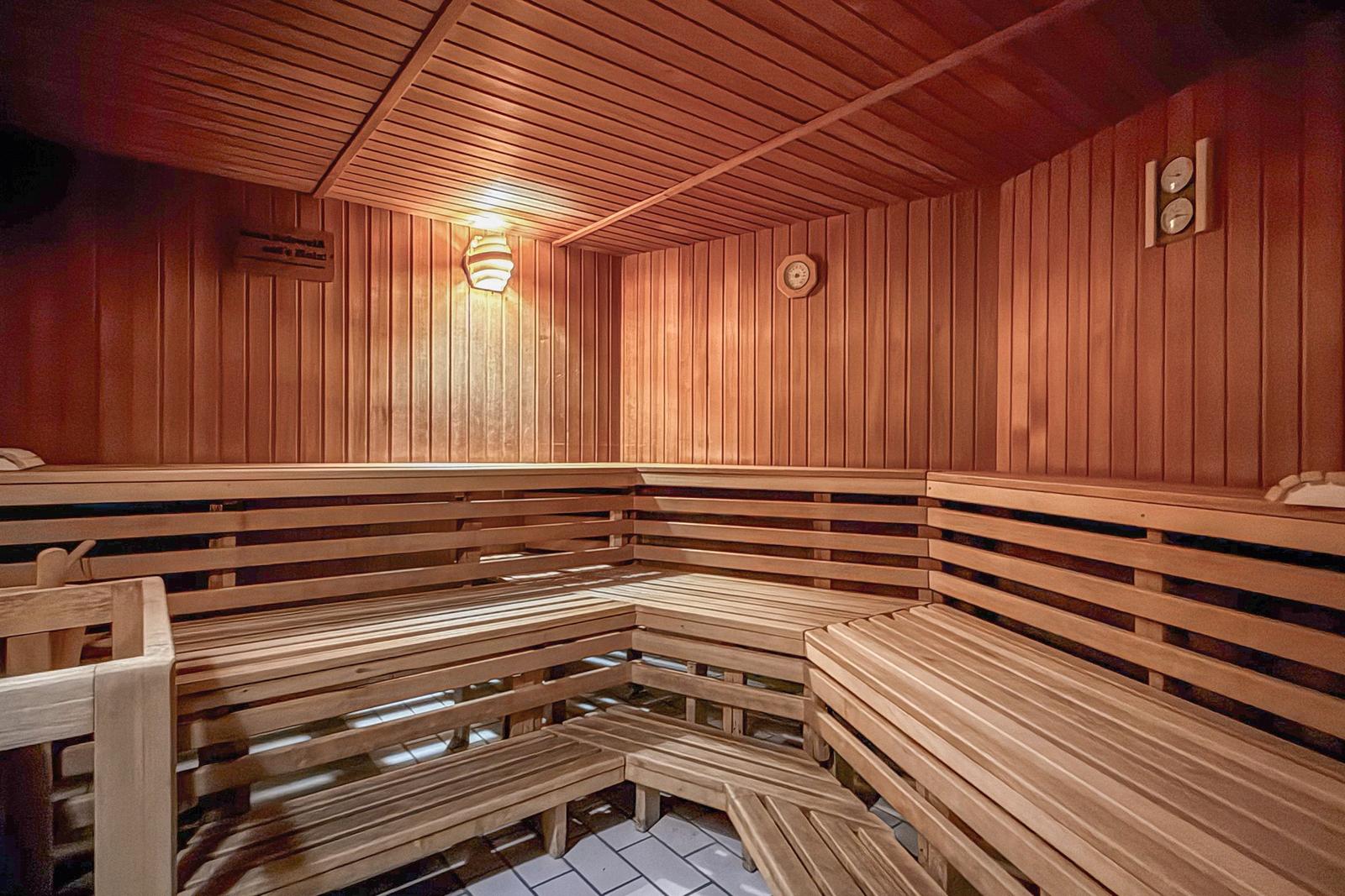 Holzsauna mit mehreren Sitzbänken und Wanduhr.