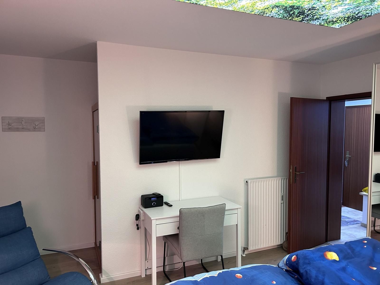 Schlafzimmer mit Schreibtisch, Fernseher und Bett unter Glasdach