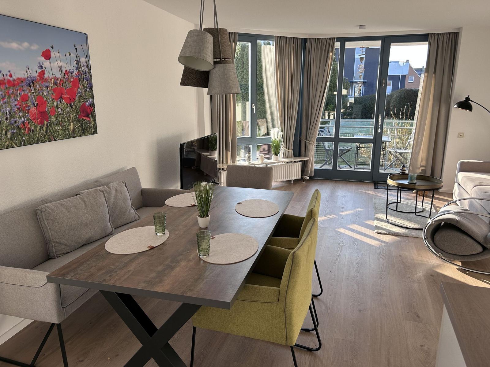 Essbereich mit Tisch, Stühlen und Blick auf Balkon. Wandbild mit Blumen.