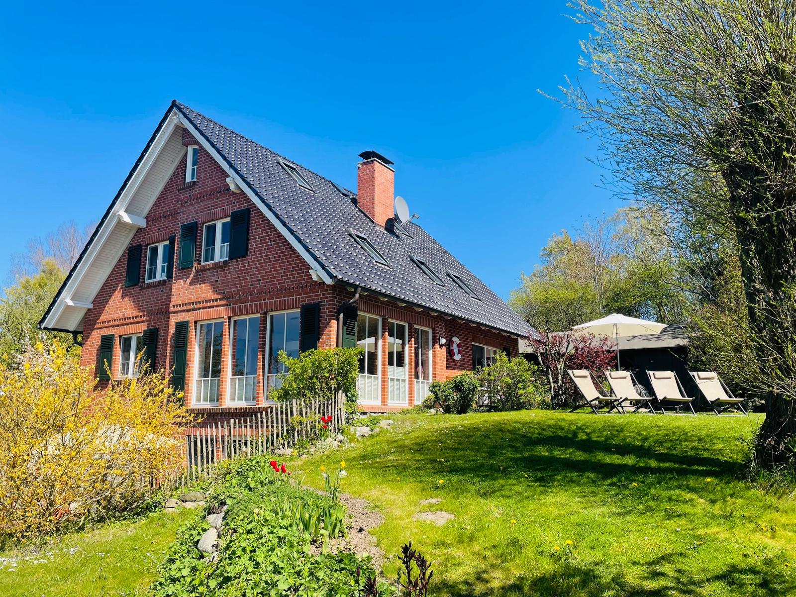 Rotes Backsteingebäude mit Dachgauben und Garten mit Liegestühlen.