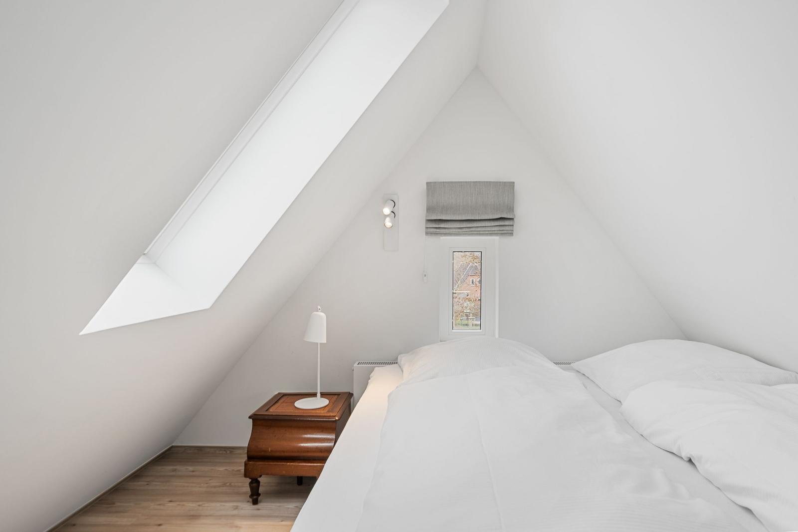 Bedroom with sloped ceiling, large skylight, bed, and nightstand.