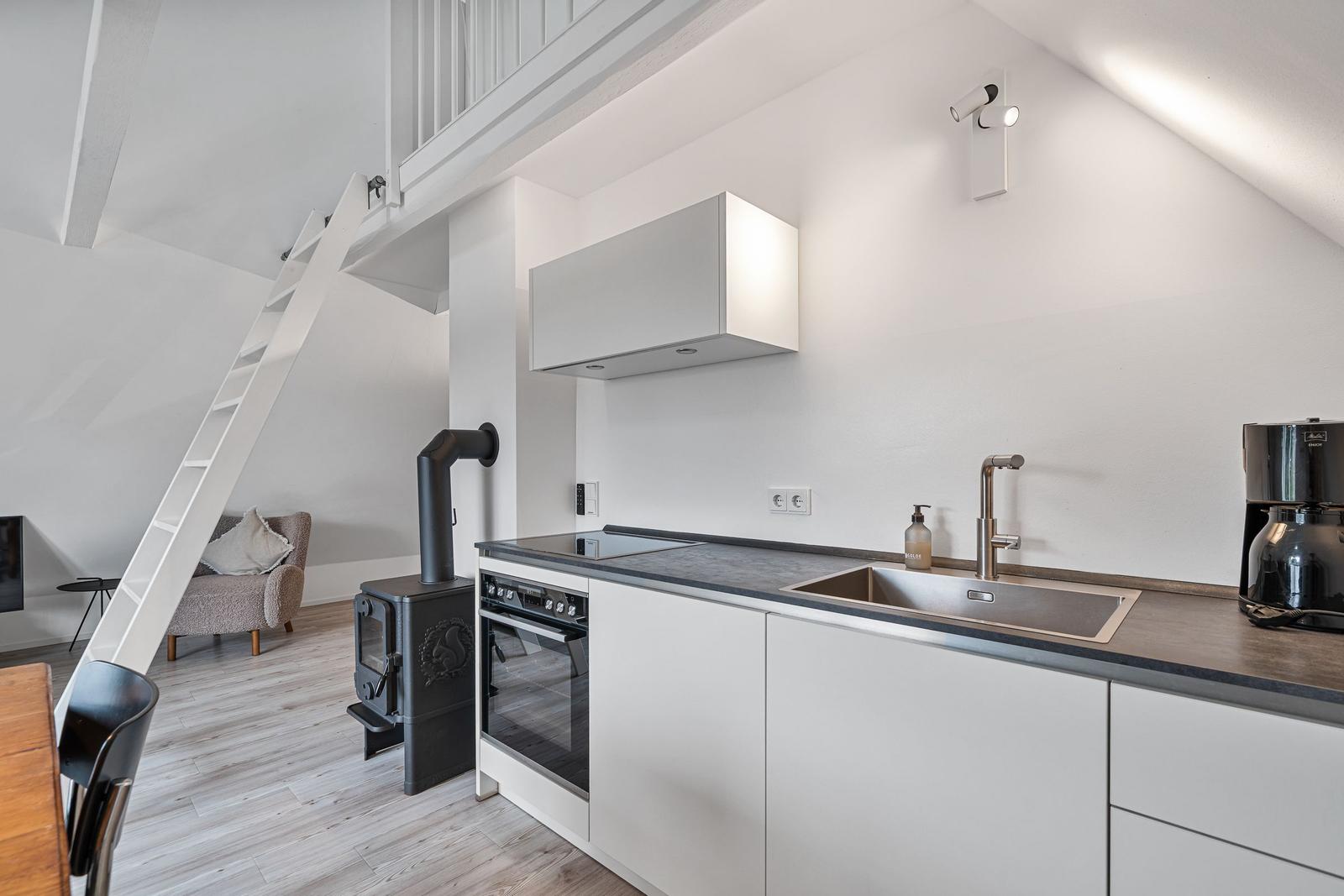 Kitchen with countertop, sink, and stove. Staircase and stove in the background.