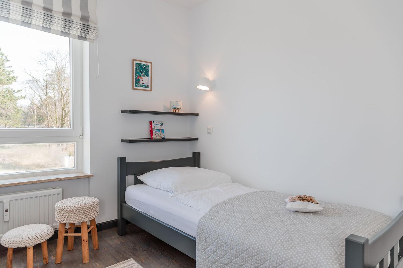 A bedroom with a bed, window, and shelves on the wall.