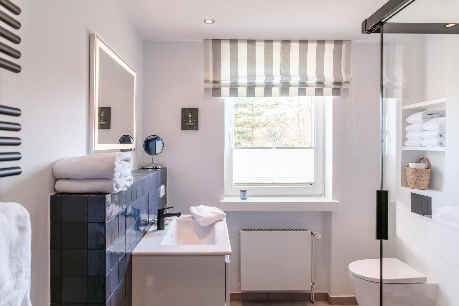 Bathroom with sink, shower, and window with striped roller blind.