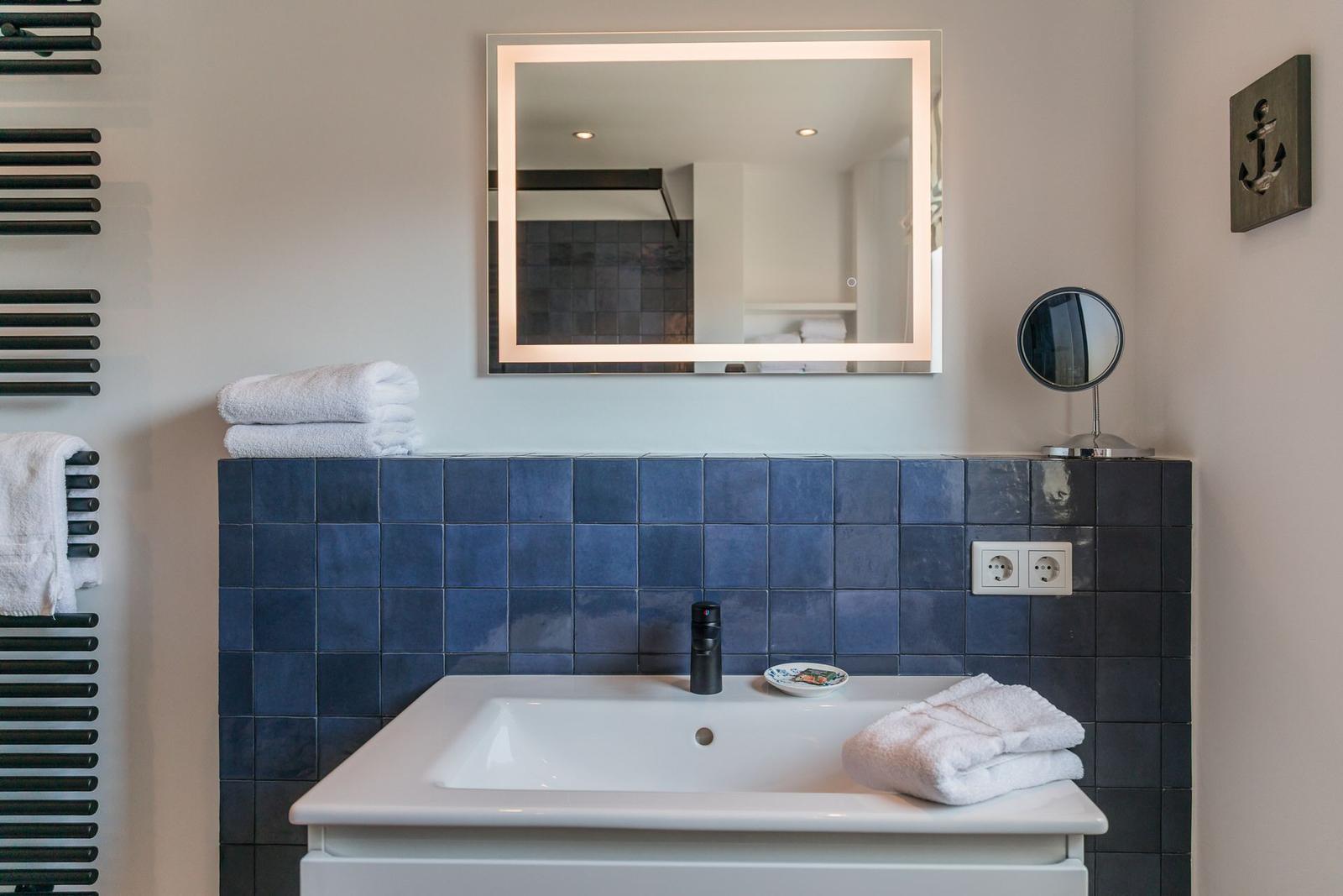 Bathroom with blue tiles, mirror, and towel radiator.