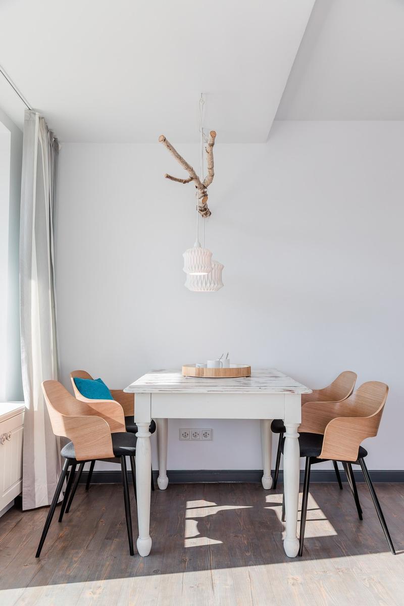 Dining room with white table, wooden chairs, and hanging lamp with branch.