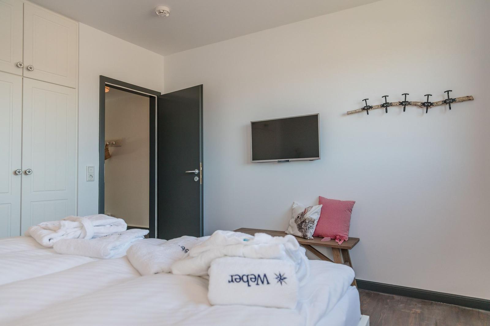 Bedroom with bed, TV, and coat hooks on the wall.