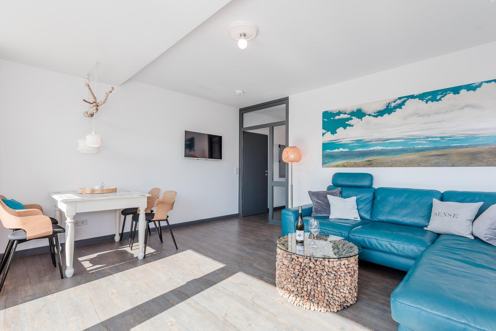 Living room with blue sofa, dining table, and wall art. Wood floor and ceiling light.