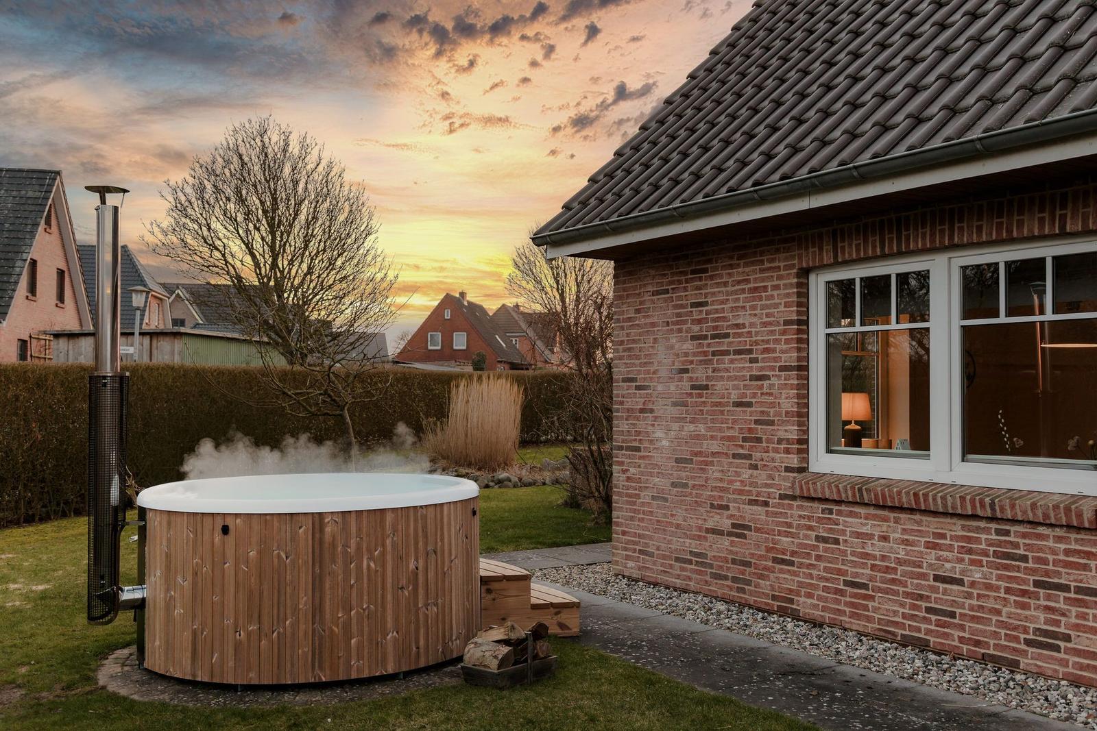 Haus mit Holzwhirlpool im Garten bei Sonnenuntergang.
