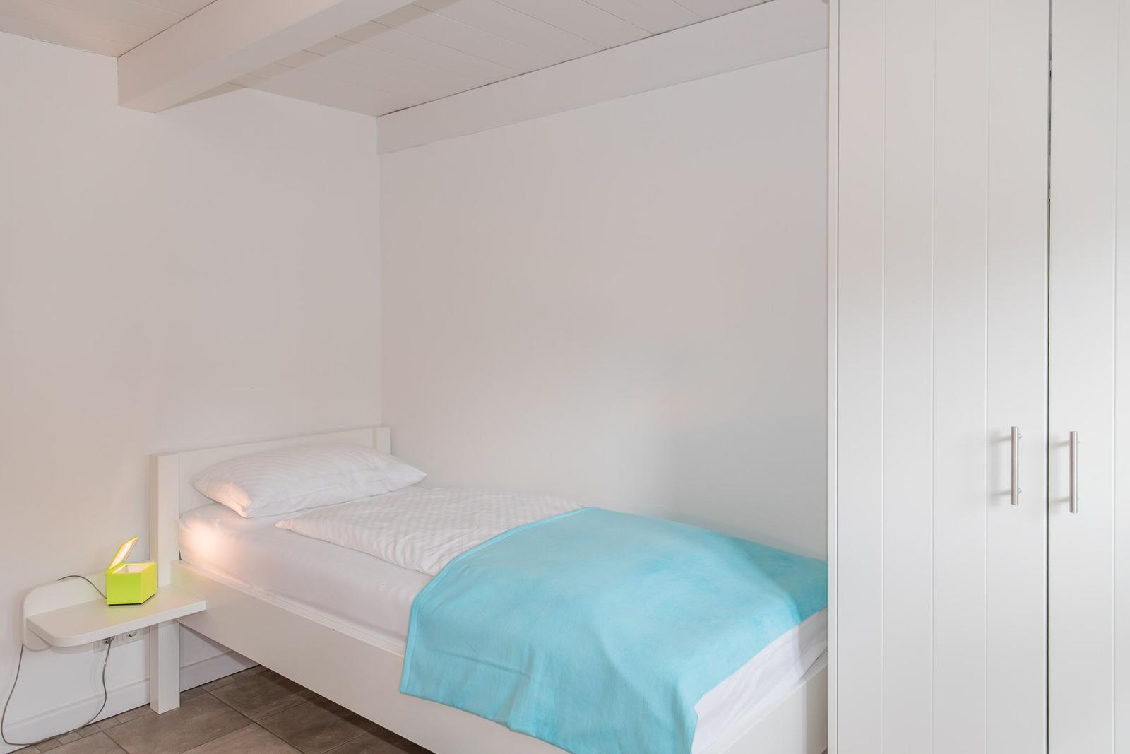 Ein Schlafzimmer mit Einzelbett, weißer Wand und Kleiderschrank.