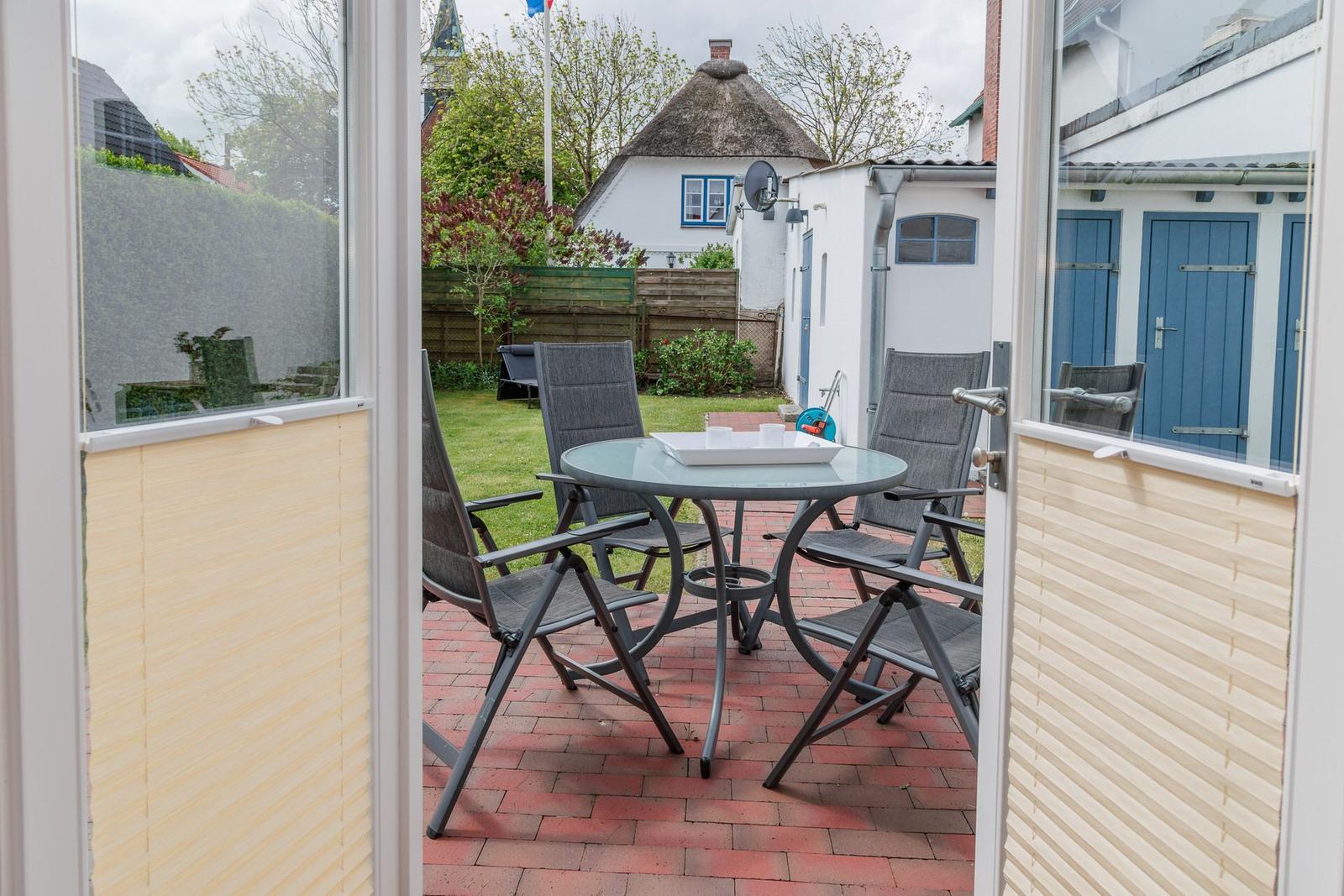 Terrasse mit Tisch und Stühlen, Blick auf Garten und Haus mit Strohdach.