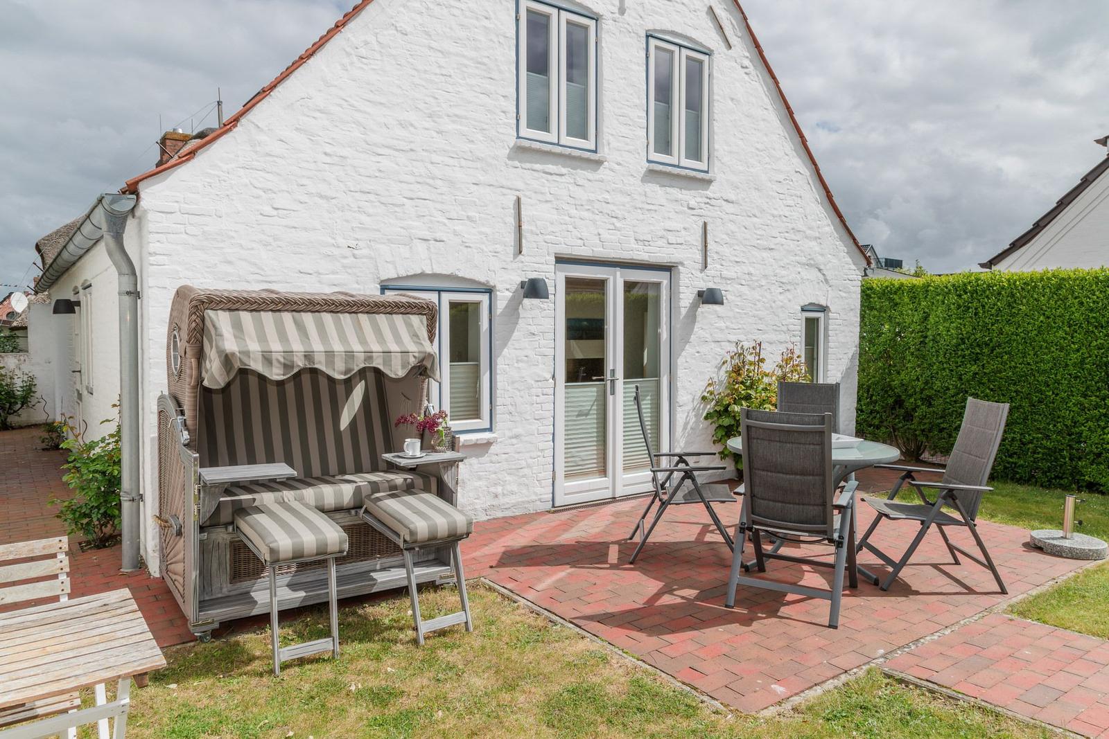 Weiße Villa mit Terrasse, Strandkorb und Gartenmöbeln.