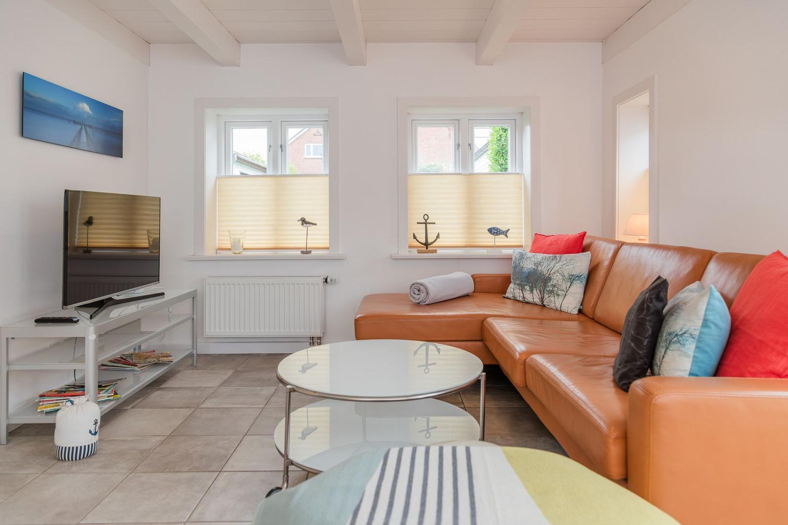 Wohnzimmer mit braunem Sofa, runden Tisch und TV. Zwei Fenster mit Jalousien.