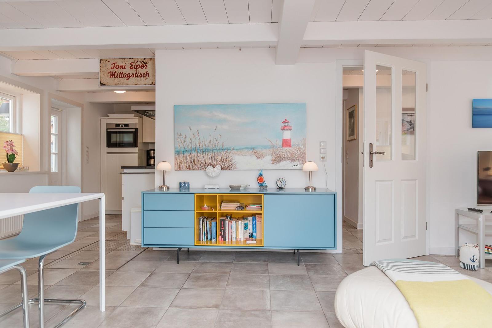 Wohnzimmer mit blauem Sideboard, Küchenbereich und Bett. Wandbild zeigt Leuchtturm.