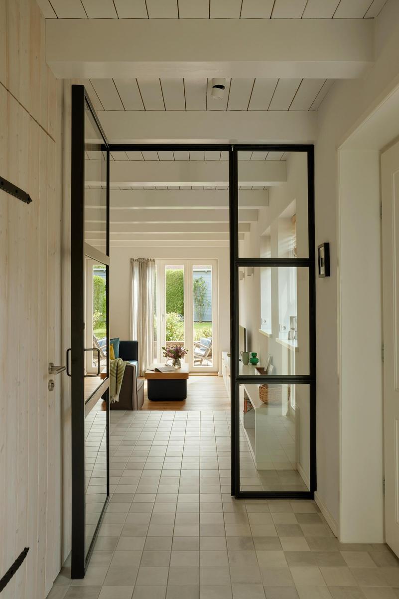 Höhenverstellbare Glaswände führen in einen hellen Wohnbereich mit Terrasse.