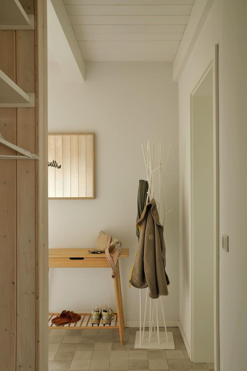 Eingangsbereich mit Kleiderständer, Holzbank und Schuhschrank. Wandbild und hell gefliestes Boden.
