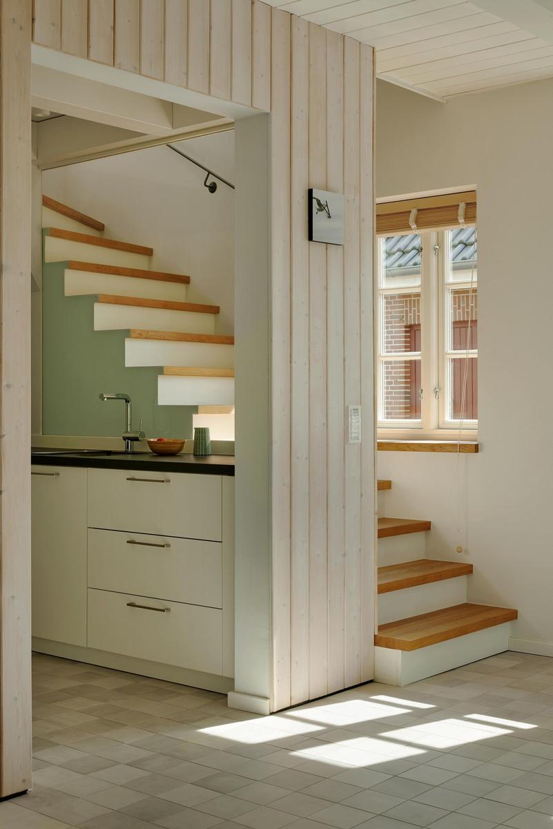 Küche mit Arbeitsplatte und Treppe zur oberen Etage. Fenster mit Holzrahmen.