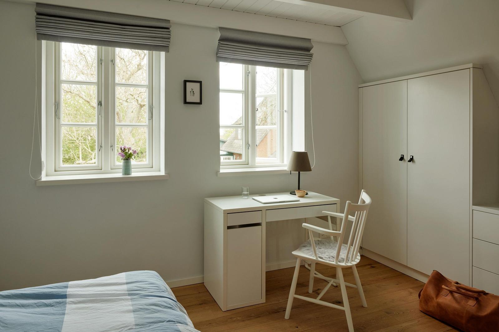 Ein Schlafzimmer mit zwei Fenstern, Schreibtisch und Kleiderschrank.