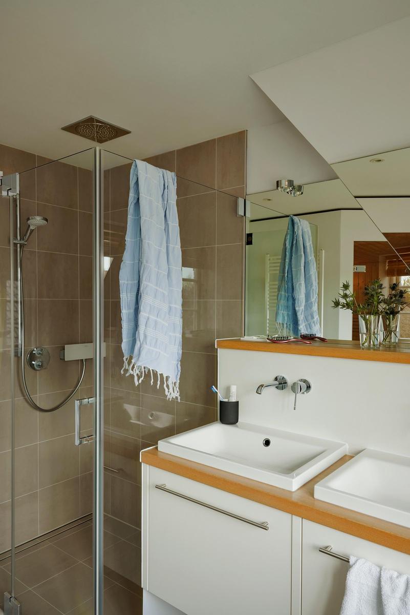 Duschkabine mit Glaswand, Waschbecken und Spiegel. Handtuch hängt an der Dusche.