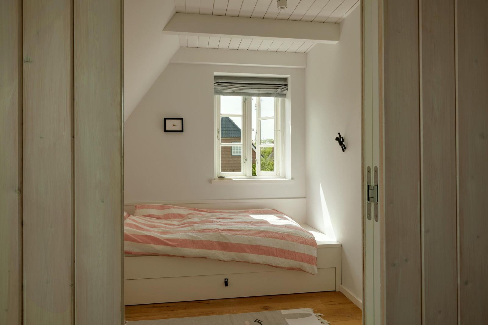 Schlafzimmer mit Dachschräge, Fenster und Bett mit Streifenbezug.