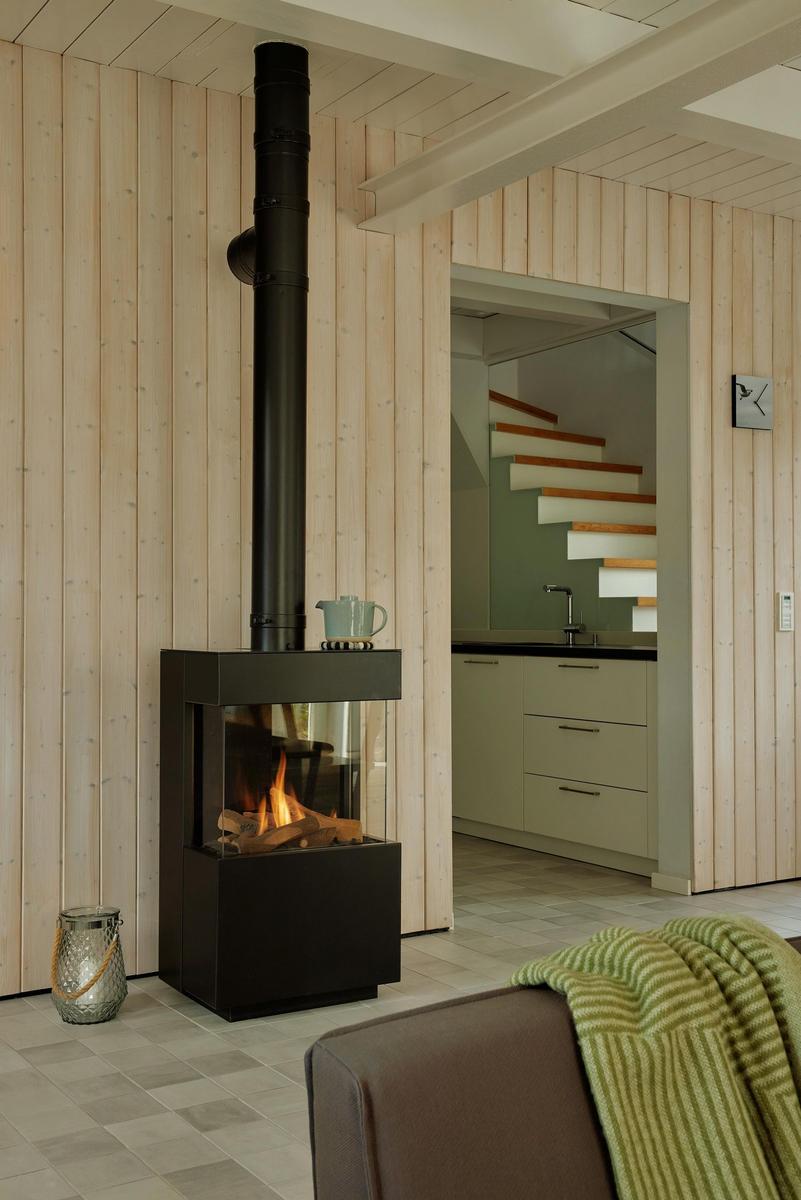 Moderne Wohnküche mit Holzwand, Kamin und Treppe im Hintergrund.