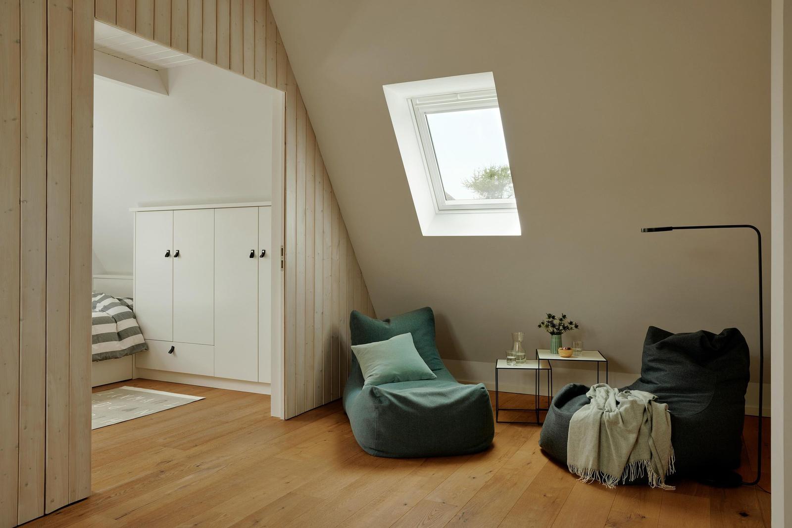 Dachgeschosszimmer mit zwei Sitzkissen, Dachfenster und Holzboden. Im Hintergrund Schlafzimmer mit Kleiderschrank.