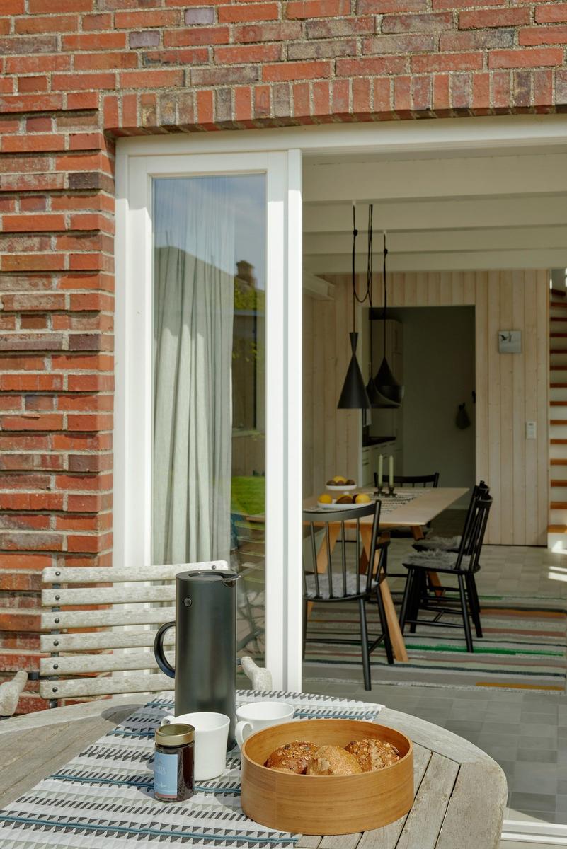 Terrasse mit Tisch, Kaffeetasse und Brot. Durch Glastür ist Esszimmer mit Tisch und Stühlen sichtbar.