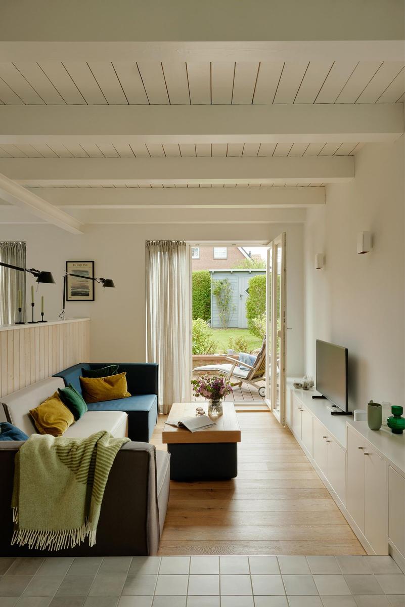 Wohnzimmer mit Sofa, Couchtisch und TV. Durchgang zur Terrasse mit Gartenansicht.