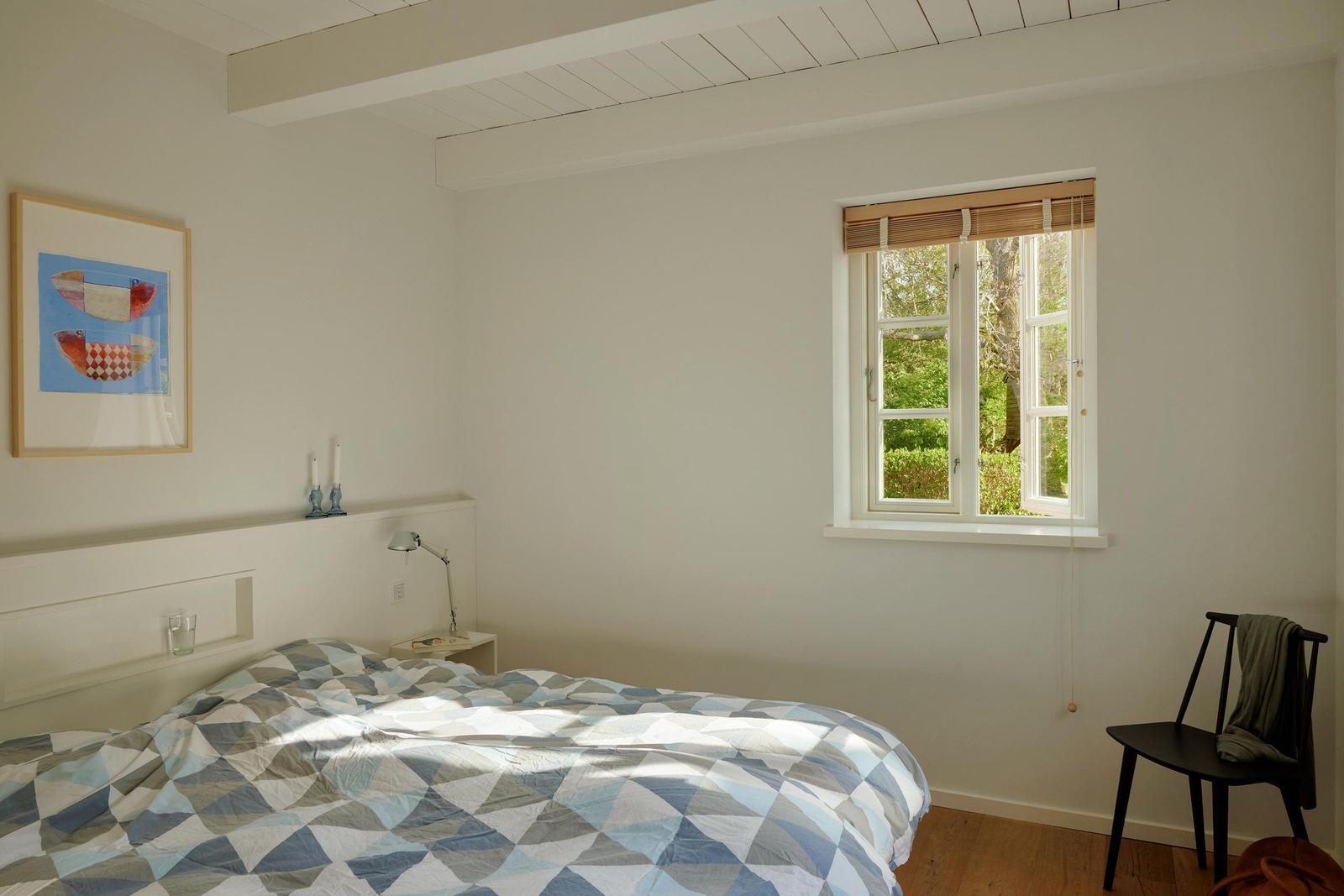 Schlafzimmer mit Bett, Fenster und Stuhl. Wandbild und Nachttisch sind sichtbar.