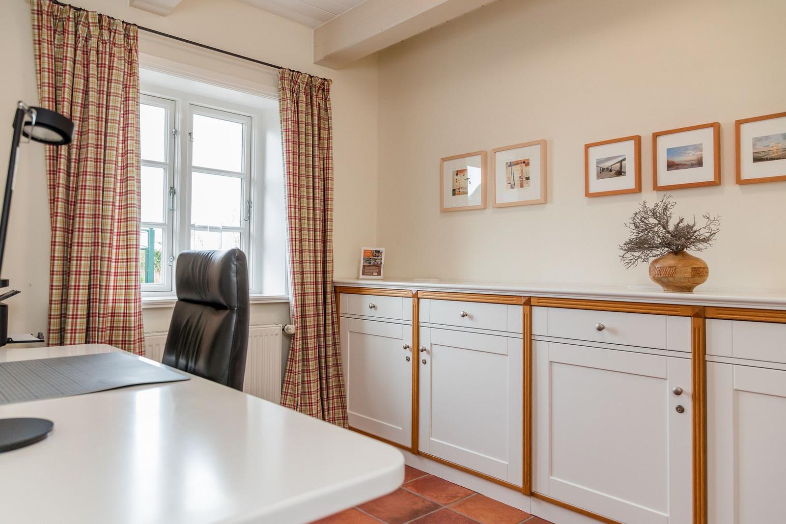 Arbeitszimmer mit Schreibtisch, Stuhl und Fenster mit Vorhängen.