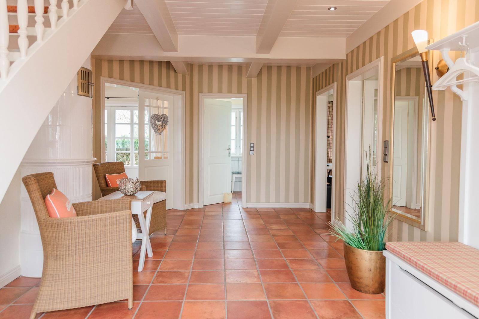 Hausflur mit Streifenwand, Terrakottboden und Sitzgelegenheit unter einer Treppe.