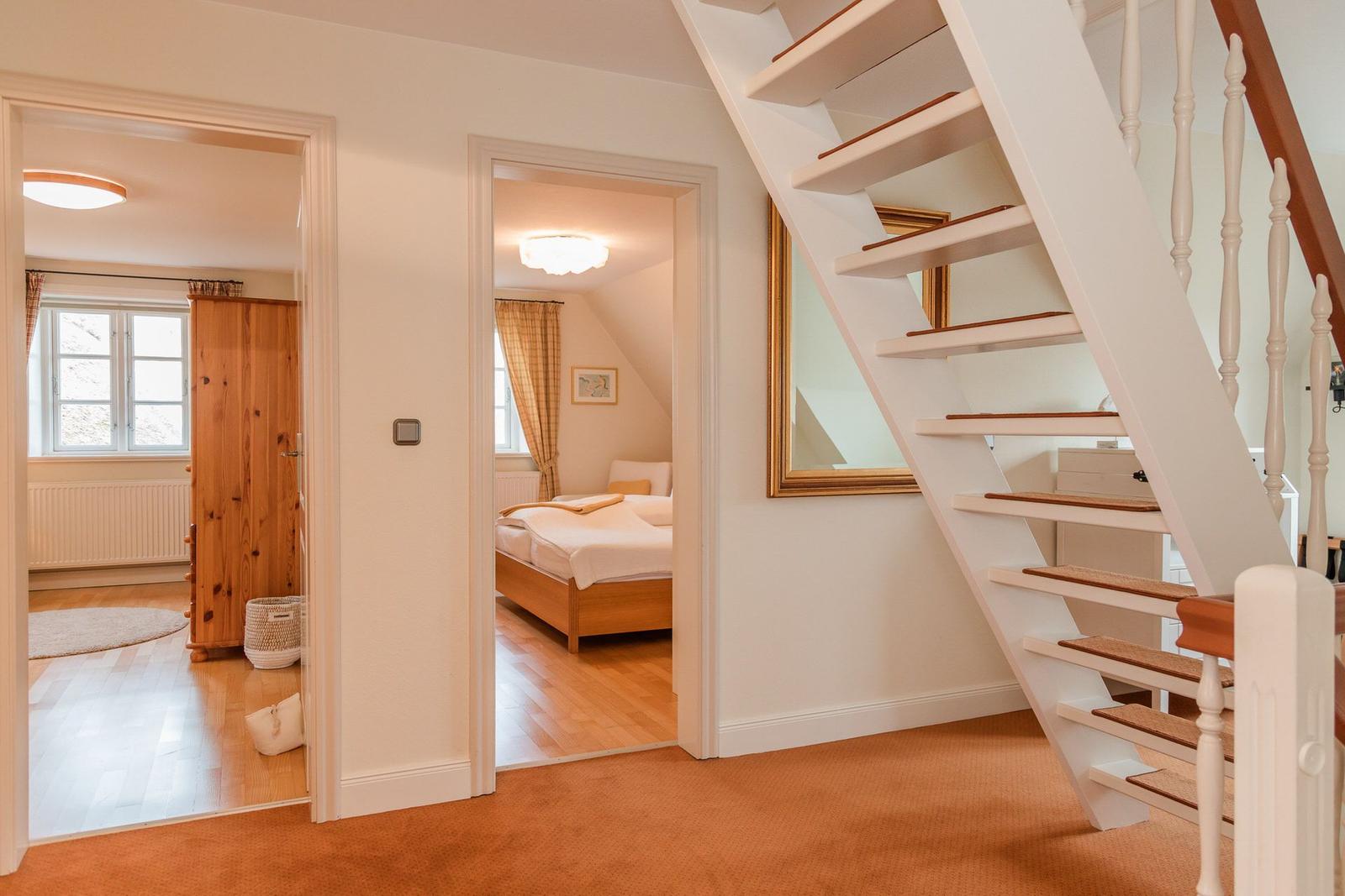 Treppenhaus mit Blick auf Schlafzimmer und Wohnzimmer mit Holzmöbeln und Fenstern.