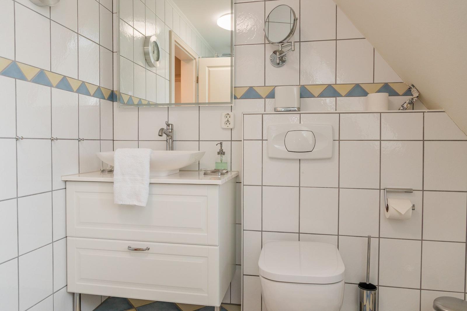 Badezimmer mit Waschbecken, Spiegel und Toilette. Wandfliesen mit dekorativer Bordüre.