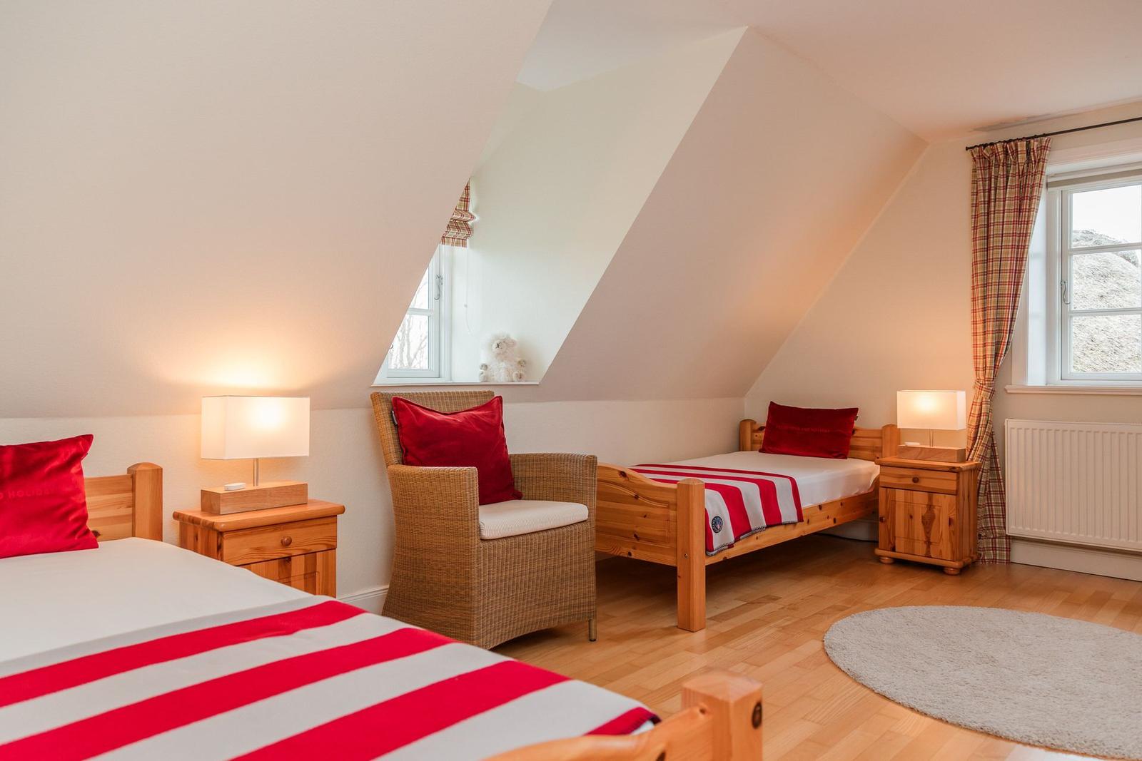 Zimmer mit zwei Betten, Stuhl und Fenstern im Dachgeschoss.
