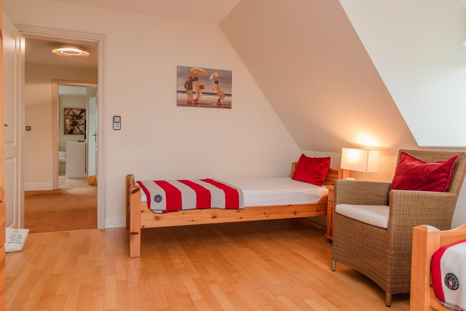 Ein Schlafzimmer mit Holzbett, Sessel und Wandbild. Holzfußboden und Dachschräge.